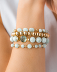 Stack of gold and white beaded bracelets on a wrist with a blurred background