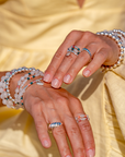 Close-up of hands wearing multiple bracelets and rings with a yellow garment in the background