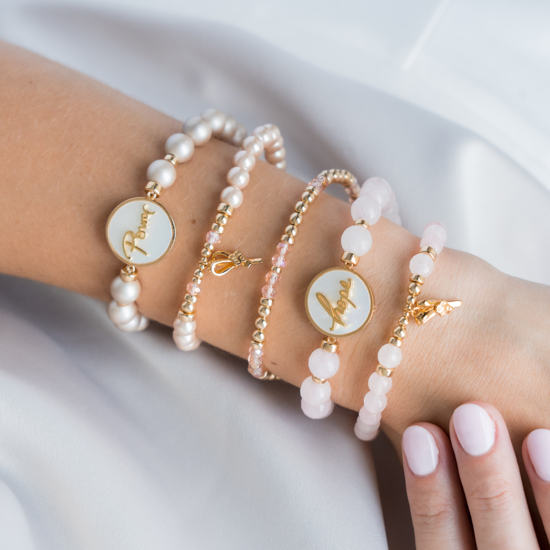 Three pearl and gold bracelets on a person's wrist against a white background