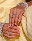 Close-up of hands wearing multiple rings and bracelets on a yellow dress background.