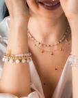 Person wearing layered necklaces in white agate with touches of color, paired with stacked bracelets, against a neutral background.