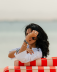 Woman sitting on a red and beige striped chair by the water, wearing a white shirt and jewelry in sterling silver and brazilian blue sodalite . made in montreal.