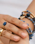 Hand wearing a stack of gold vermeil rings and blue sodalite beaded bracelets on a white background/ beblue bijoux