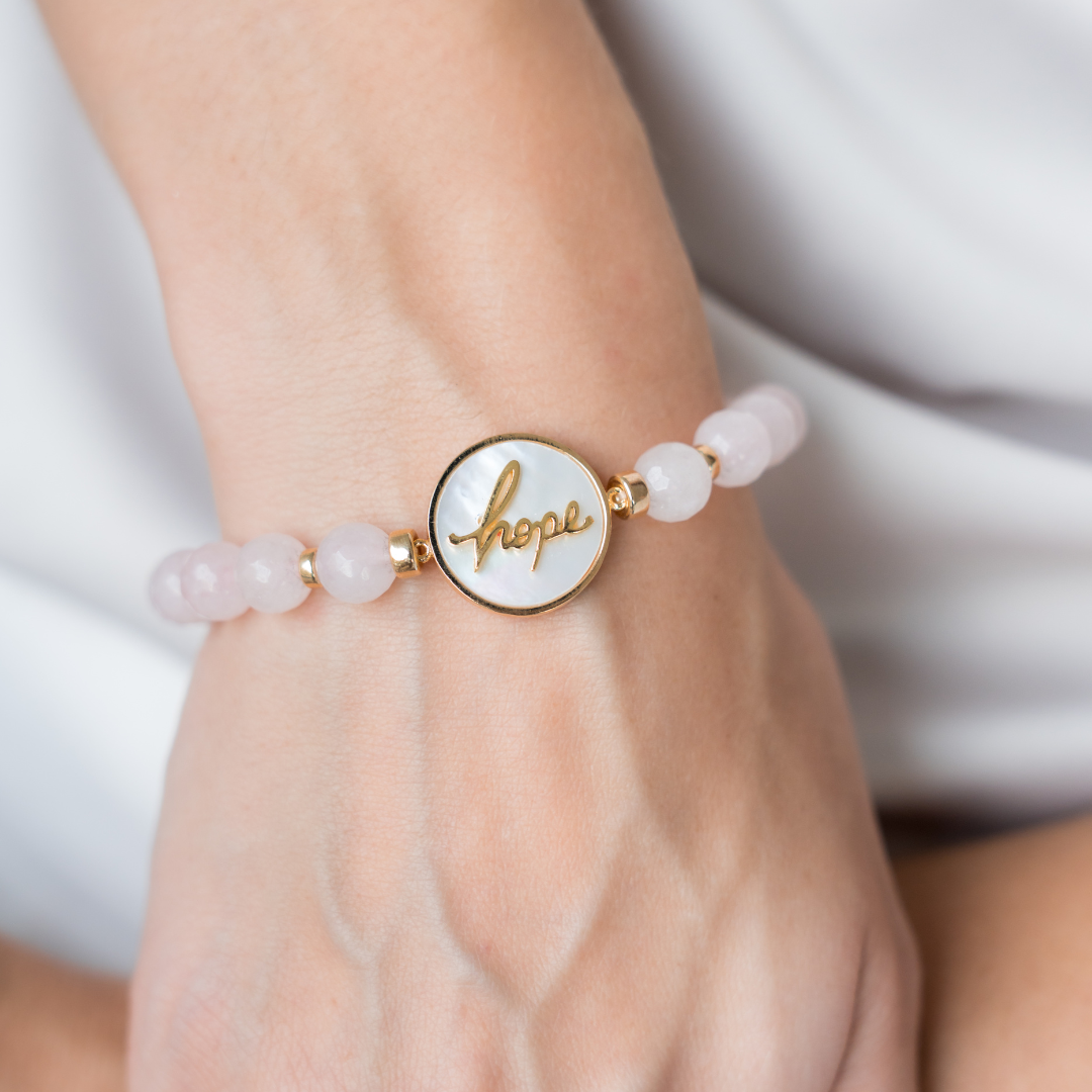 Bracelet with 'hope' charm on a wrist against a neutral background
