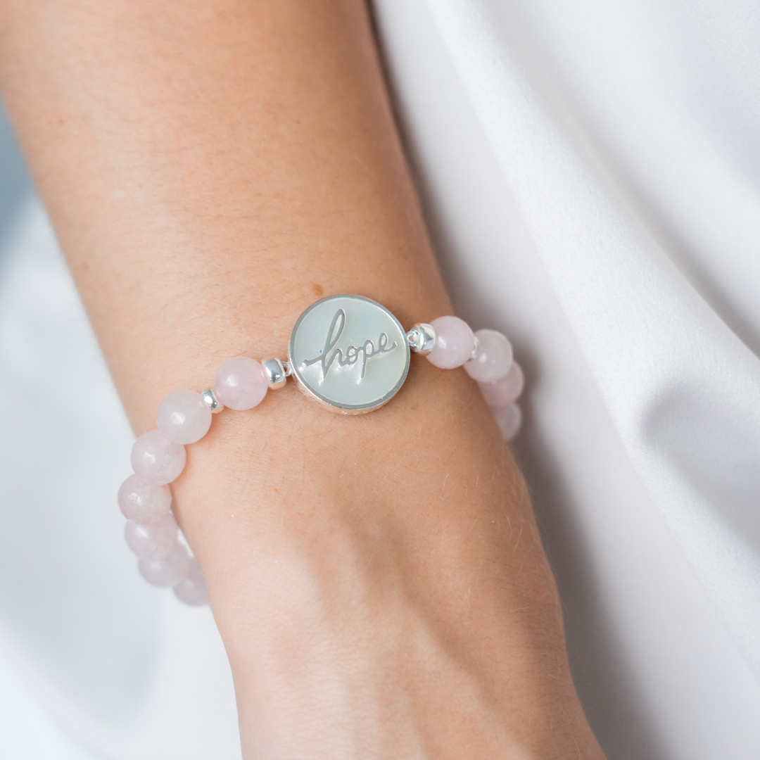 Bracelet with pink beads and a silver disc on a wrist against a white background