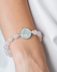 Bracelet with pink beads and a silver disc on a wrist against a white background