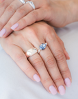 Hand wearing a stack of silver rings, including a blue sodalite elastic ring, on a white shirt. / beblue bijoux