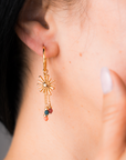 Gold earring with sun design and colorful beads worn by a woman