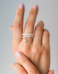 Hand wearing multiple pearl rings on a neutral background
