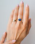 Hand wearing a stack of gold vermeil, including a blue sodalite elastic ring, on a white shirt. / beblue bijoux