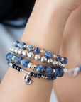 Stack of blue beaded bracelets in blue sodalite and sterling silver on a wrist with a blurred background