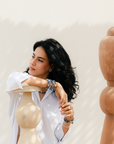 Woman in a white shirt leaning on a wooden mannequin against a plain background.She is wearing blue sodalite elastic bracelets.