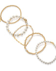 A person's hand showcasing a set of pearl bracelets with varying designs, worn on a white sleeveless top.
