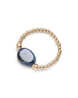 Hand wearing a stack of gold vermeil, including a blue sodalite elastic ring, on a white shirt. / beblue bijoux