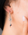 Close-up of a person wearing a silver earring with colorful beads and sun charm.