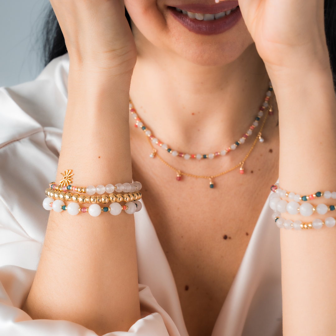 Person wearing layered necklaces in white agate with touches of color, paired with stacked bracelets, against a neutral background.
