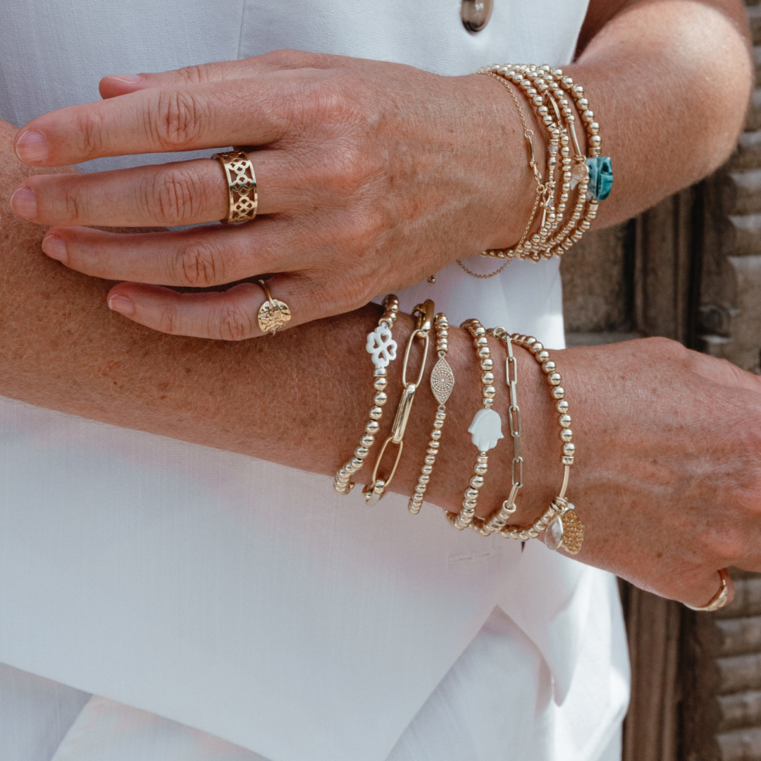 Close-up of a person's hands wearing multiple gold bracelets and rings.