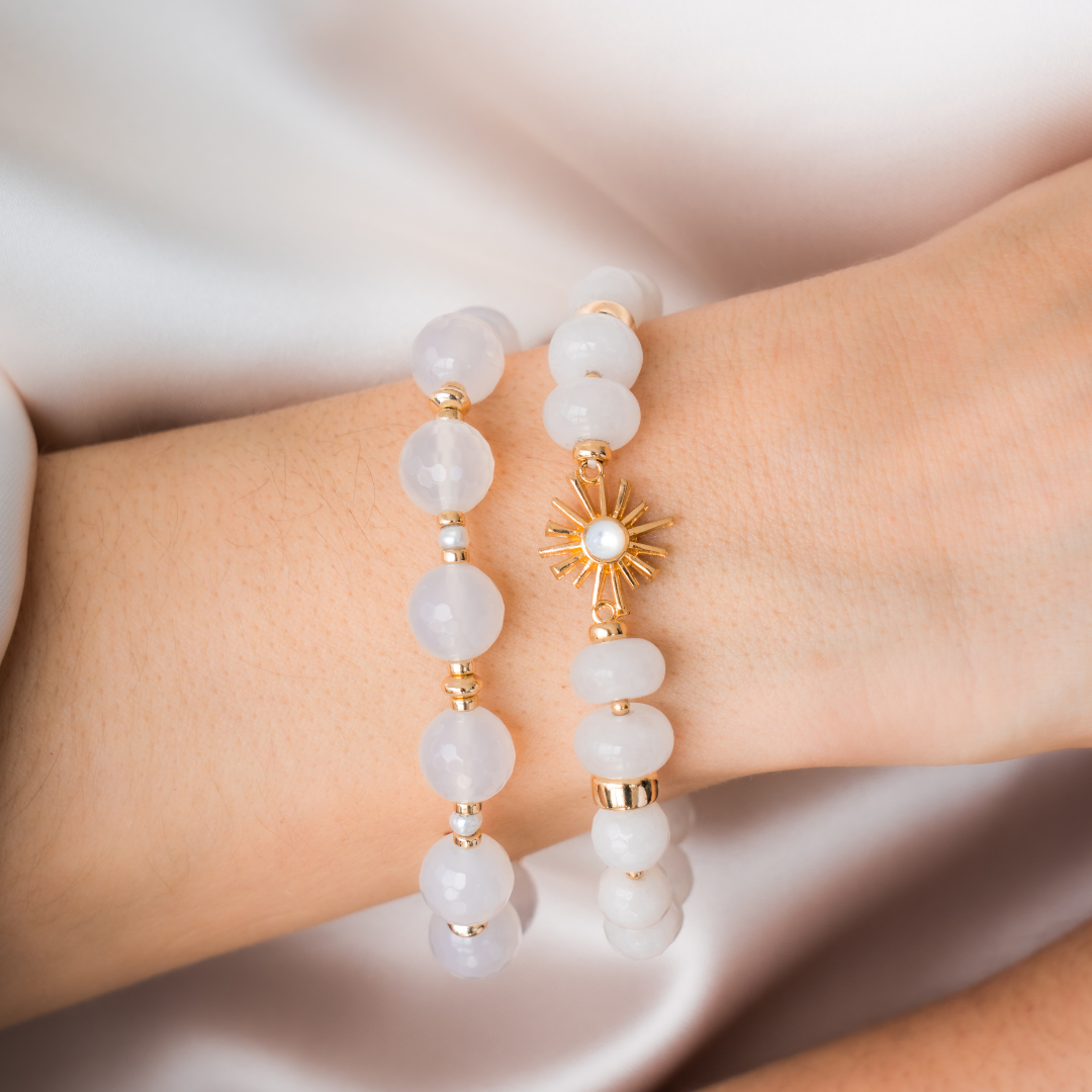 White beaded bracelet with gold accents  and sun charm on a wrist against a neutral background