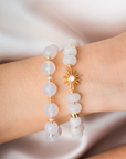 White beaded bracelet with gold accents  and sun charm on a wrist against a neutral background