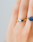 Hand wearing a gold ring with a zircon and an other elastic ring with a blue sodalite stone on a neutral background / beblue bijoux