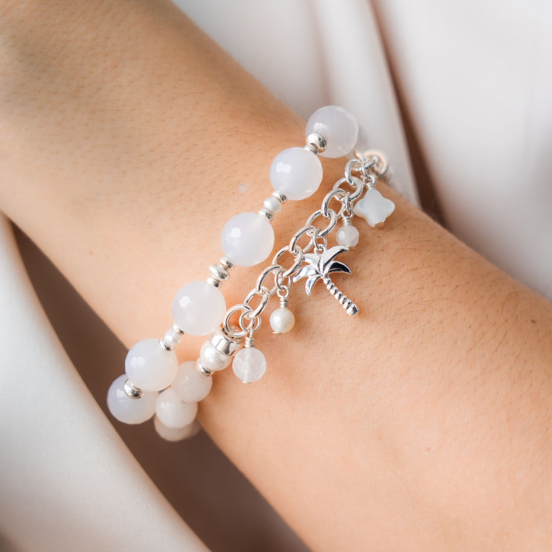 Bracelet with white beads and a palm tree charm on a wrist.
