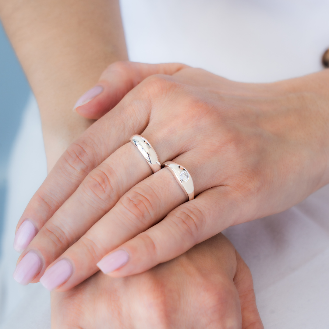 Close-up of two hands with silver rings on a neutral background
