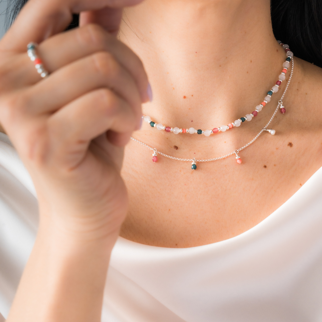 Close-up of a person wearing delicate necklaces made of white agate with touches of color from small beaded charms, set in sterling silver.