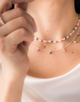 Close-up of a person wearing delicate necklaces made of white agate with touches of color from small beaded charms, set in sterling silver.