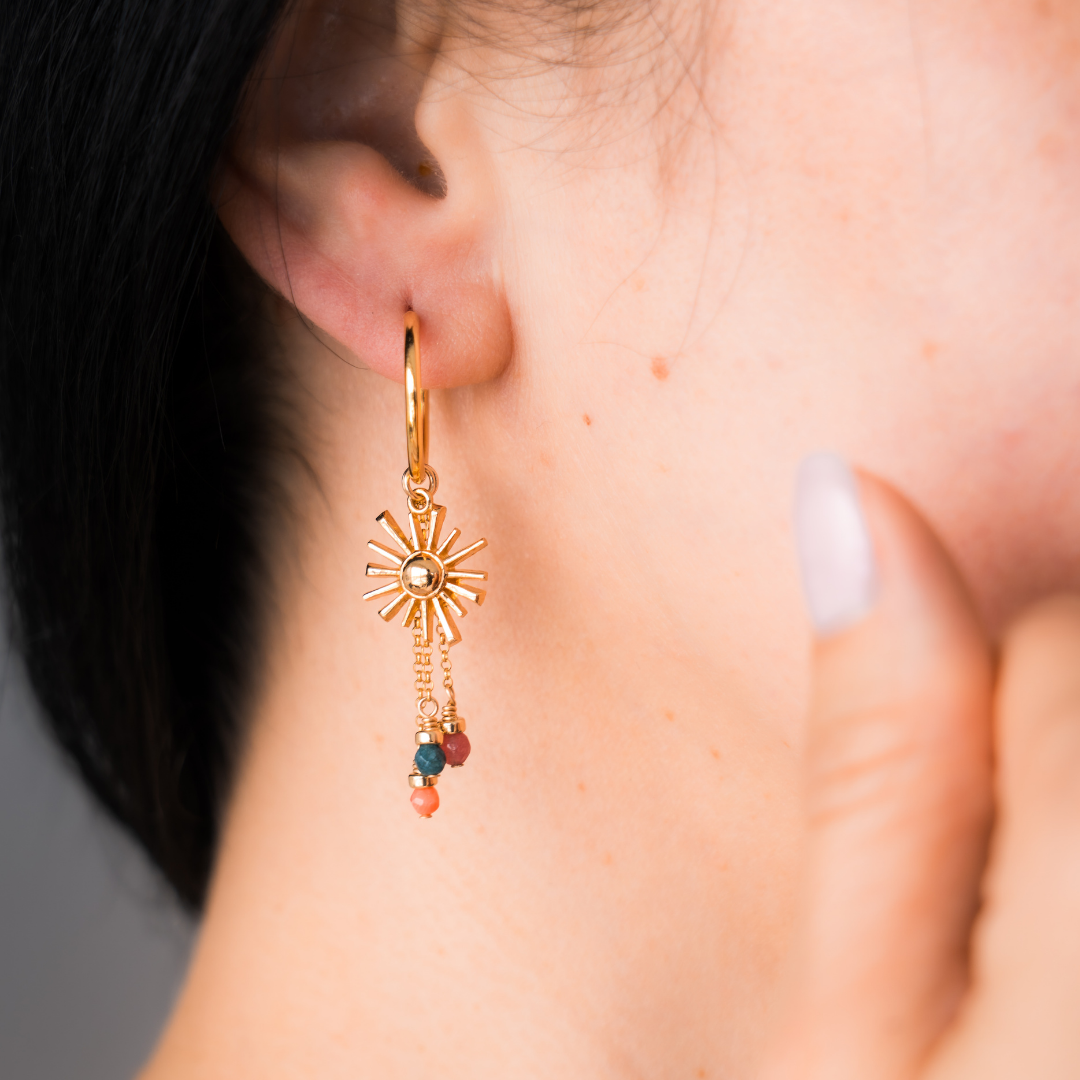 Gold earring with sun design and colorful beads worn by a woman