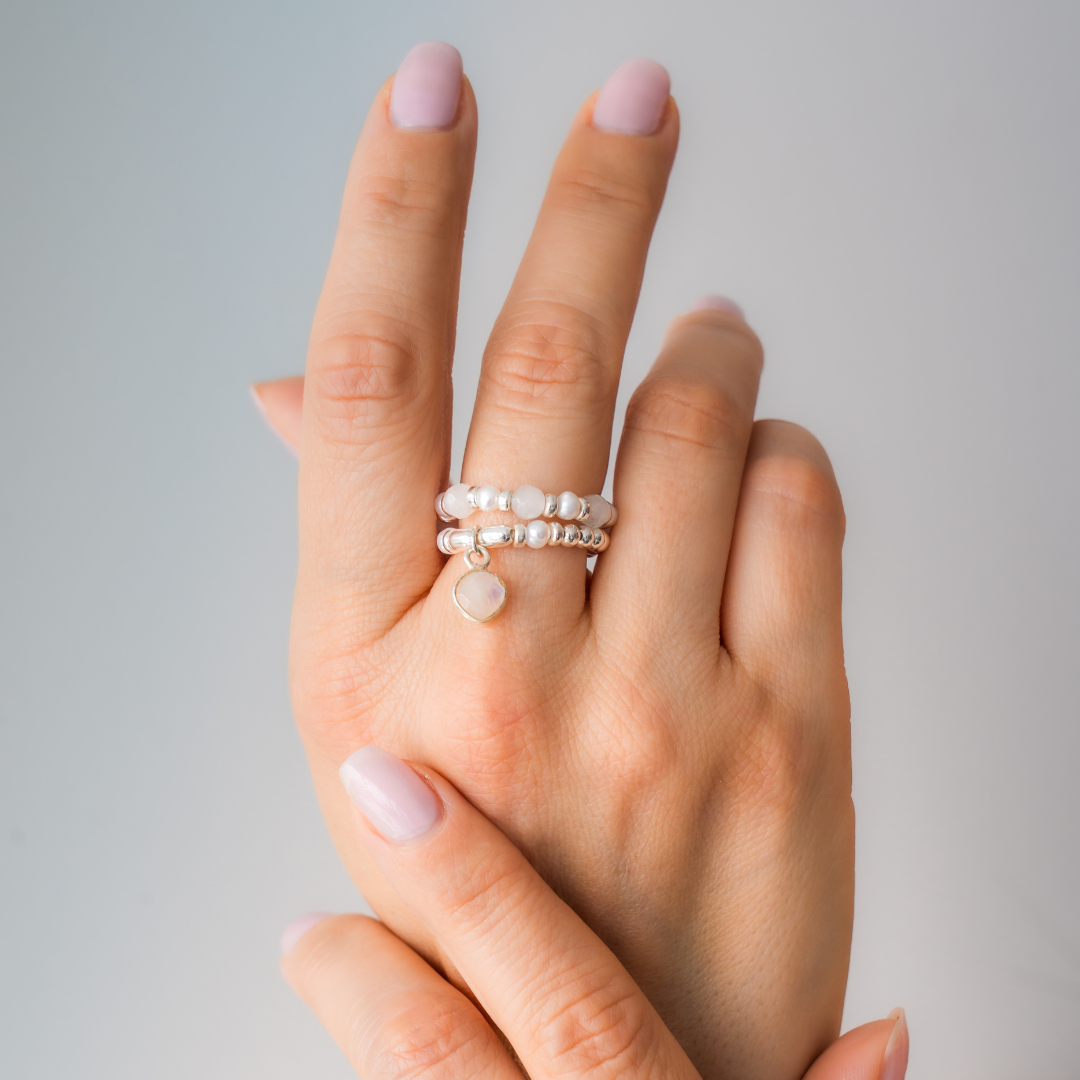 Hand wearing multiple pearl rings on a neutral background