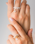 Close-up of a hand wearing multiple pearl rings and charm ring on a neutral background