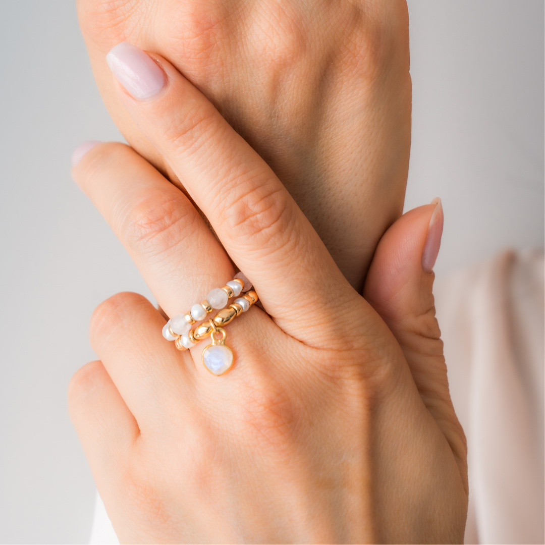 Close-up of a hand wearing stacked elastic rings in white tones, set against a light gray background.

