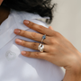 Hand wearing a stack of silver rings, including a blue sodalite elastic ring, on a white shirt. / beblue bijoux