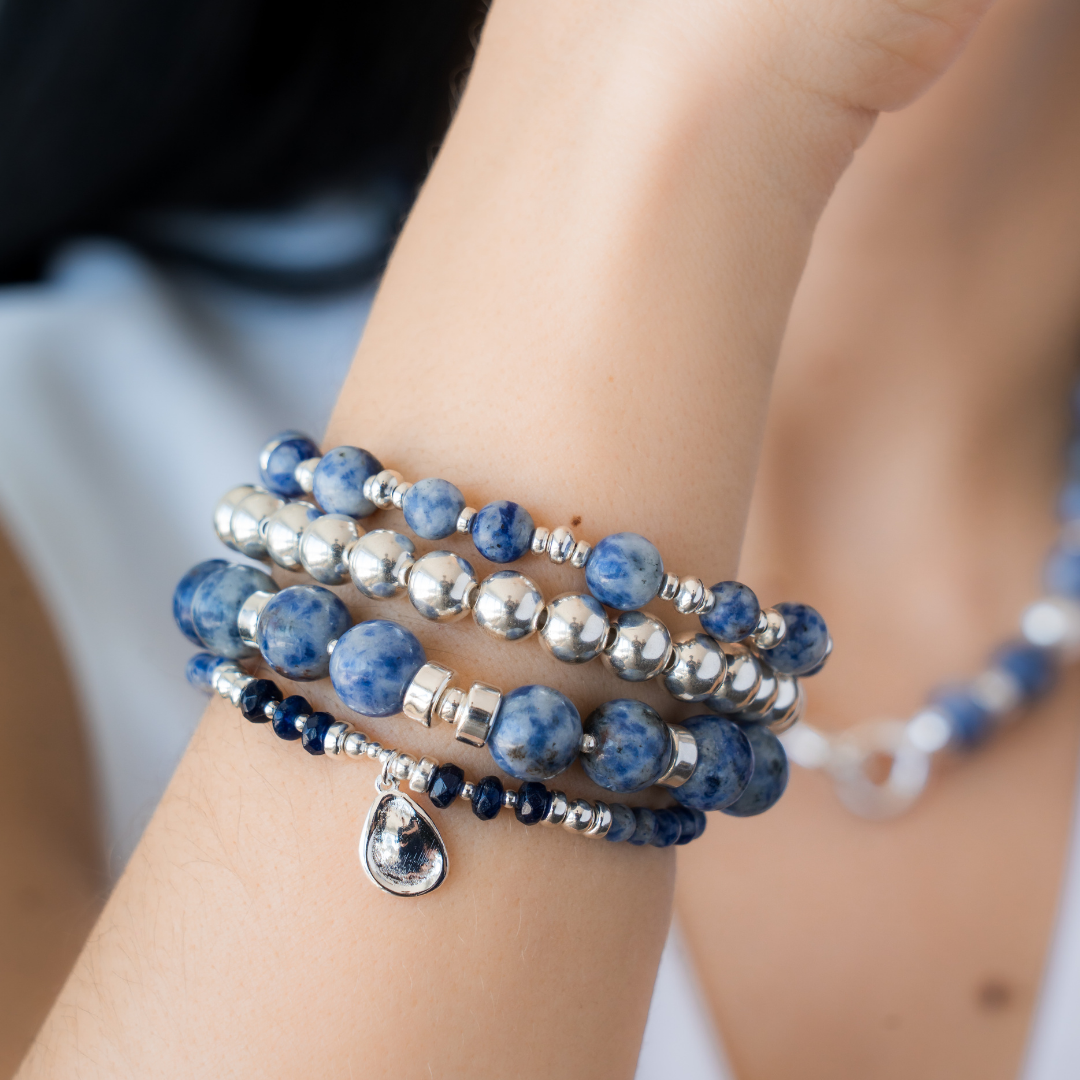Stack of blue beaded bracelets in blue sodalite and sterling silver on a wrist with a blurred background