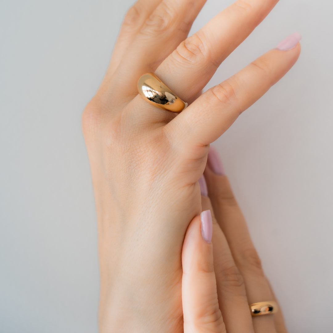 Hand wearing a gold ring on a plain background