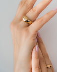 Hand wearing a gold ring on a plain background