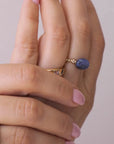 Hand wearing a stack of gold vermeil rings, including a blue sodalite elastic ring, on a white shirt. / beblue bijoux