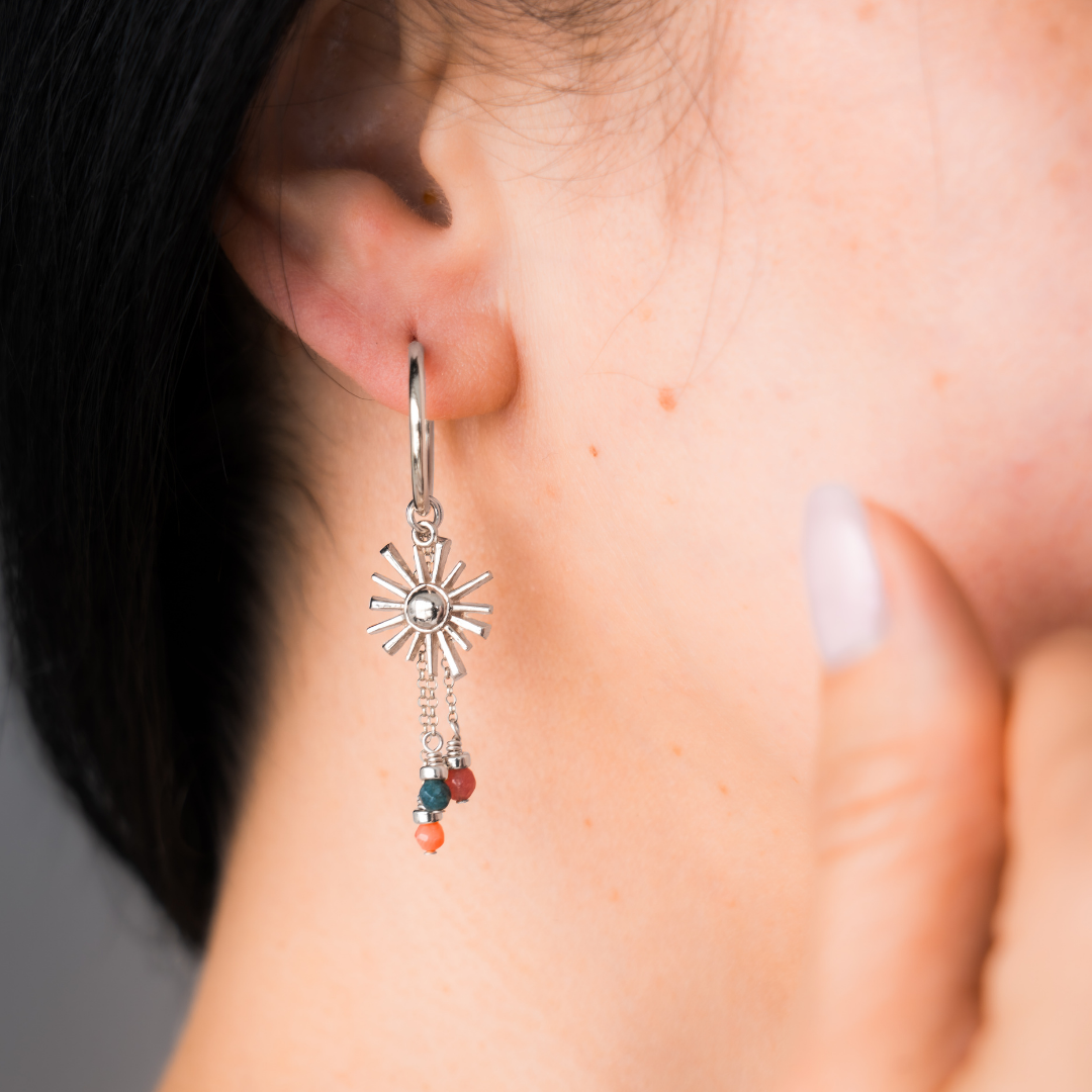 Close-up of a person wearing a silver earring with colorful beads and sun charm.